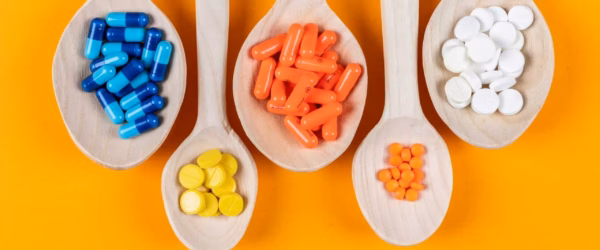 Top view colorful pills in wooden spoons on orange background. horizontal