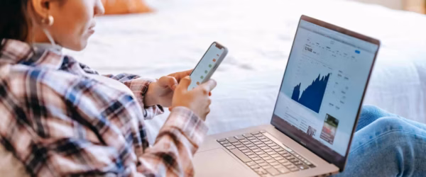 crop ethnic trader with smartphone and laptop on bench indoors