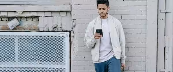 trendy indian man in earbuds chatting on smartphone in town