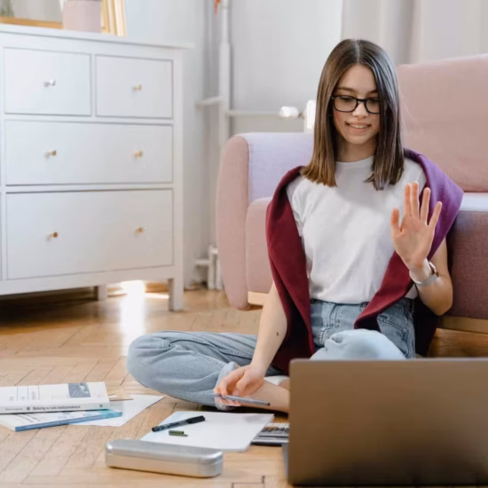a woman in white shirt sitting on the floor while talking in front of her laptop