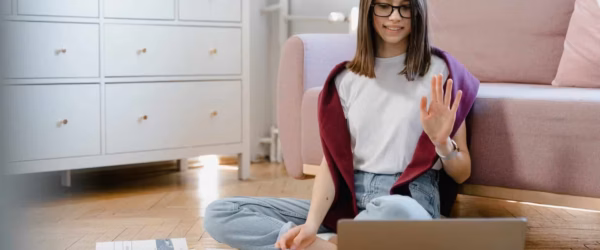 a woman in white shirt sitting on the floor while talking in front of her laptop