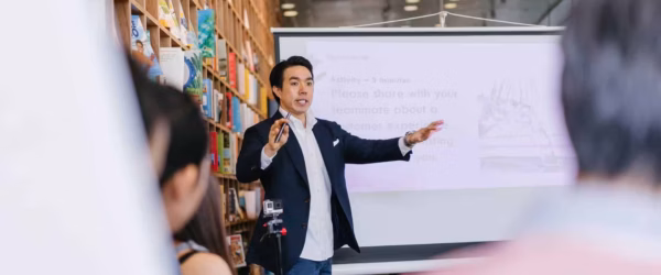 man in suit jacket standing beside projector screen