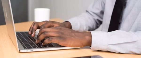 person wearing white dress shirt and black necktie using macbook air on beige wooden table