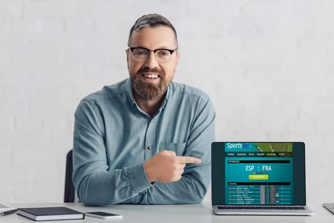 handsome businessman in shirt pointing with finger at laptop with sports bet website