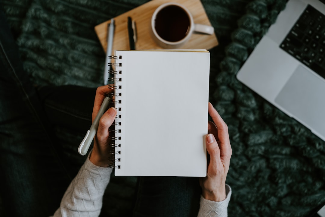 Person writing in journal notebook with coffee and laptop demonstrating daily writing practice