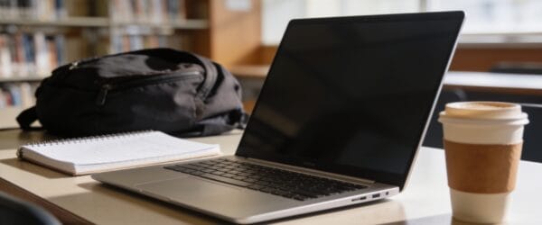College student laptop on a library desk with notebook and coffee