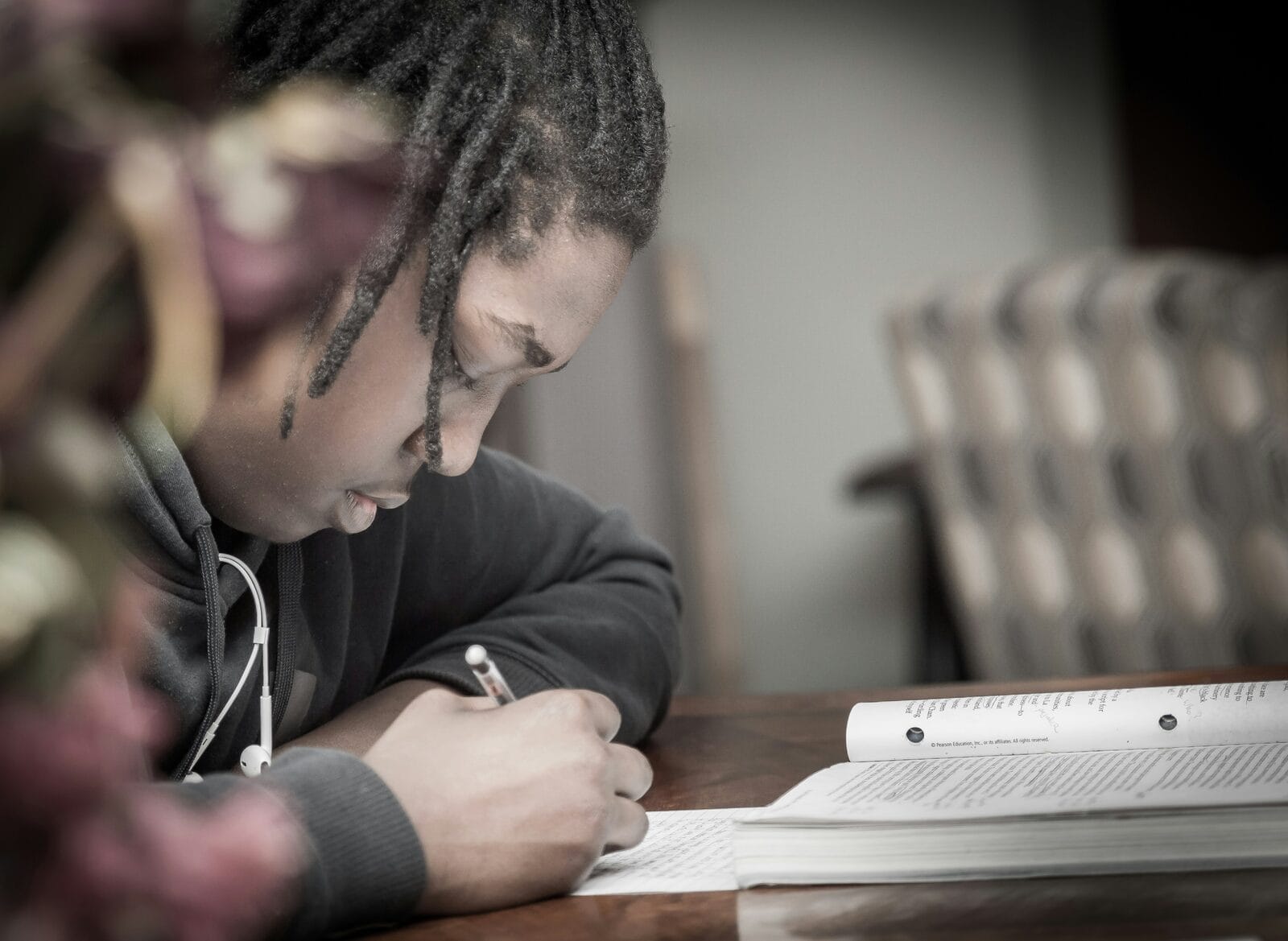 A student working through MCAT practice problems on paper beside an open review book