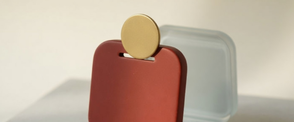 Best one-time purchase Mac apps: a brick-red porcelain tile shaped like a Mac app icon takes a single brass token through a slot, while a frosted-glass twin fades into the background