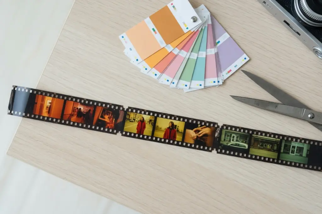 Three strips of film laid end to end like a timeline on a wooden desk, with scissors, color grade swatch cards and the corner of a camera