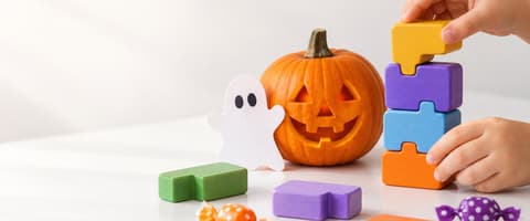 A child stacking colorful toy coding blocks next to a carved jack-o-lantern and a paper ghost on a white table